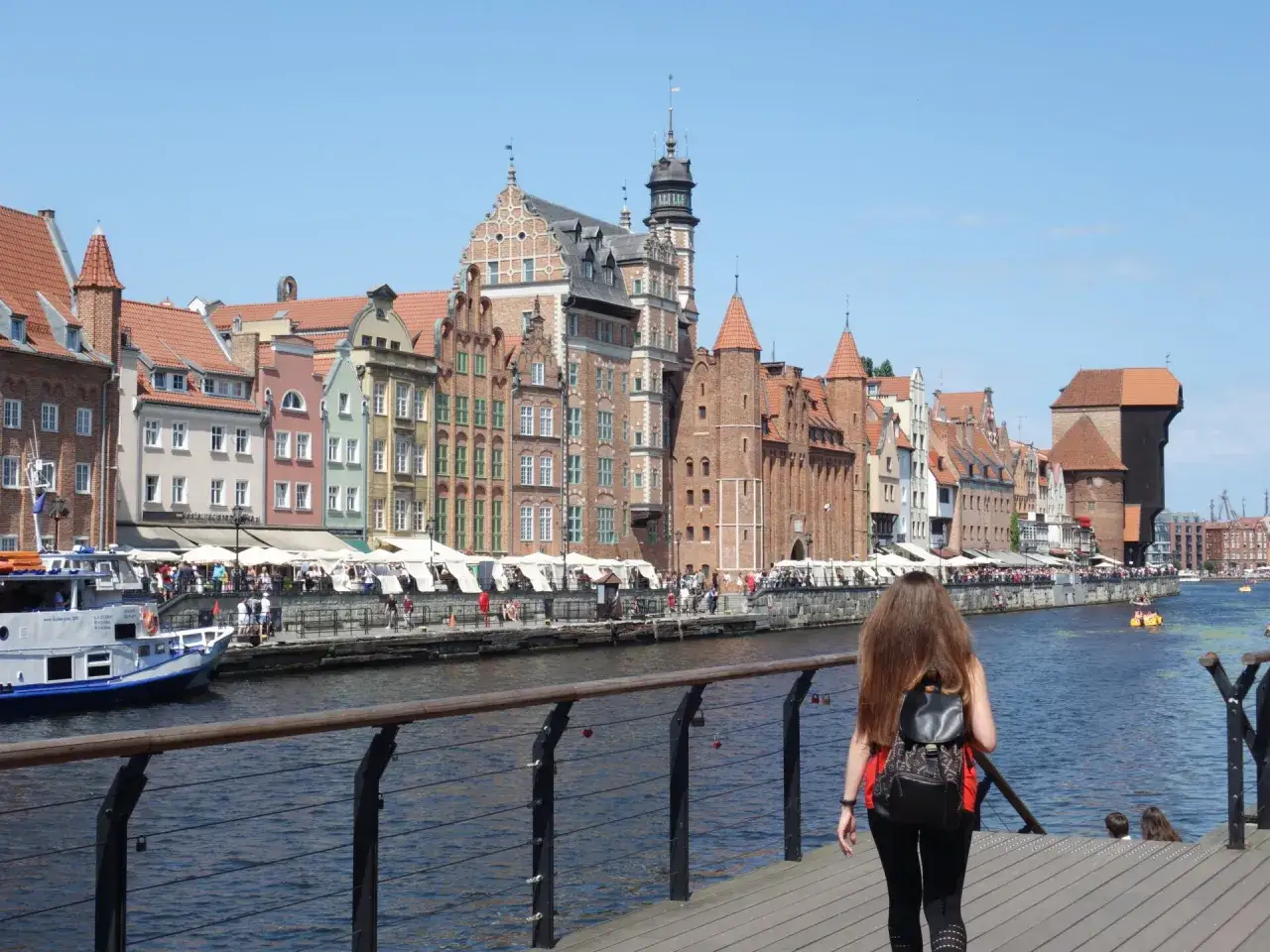 Spacer po Motławie w pięknym, słonecznym dniu. W tle widać urokliwe kamieniczki i Żuraw, charakterystyczne dla **starego miasta Gdańska**.