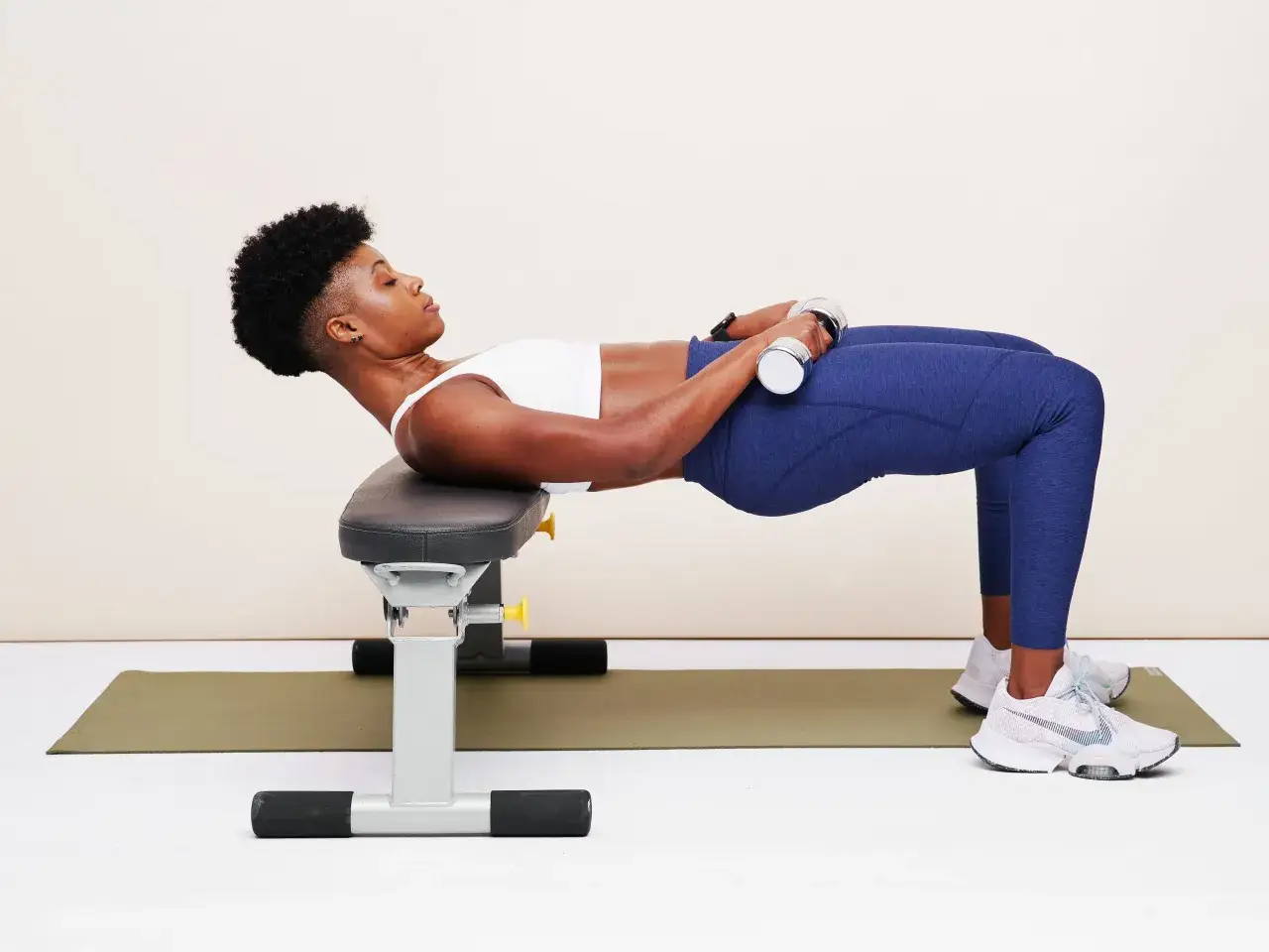Femme effectuant un hip thrust maison avec haltères sur un banc, pour renforcer ses fessiers.