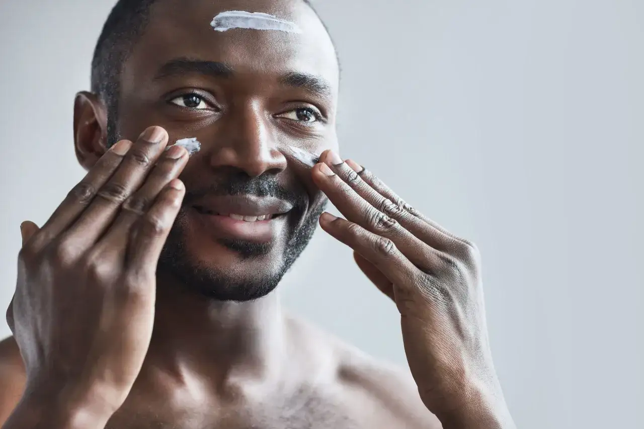Visage homme 50 ans appliquant une cr&egrave;me hydratante sur son visage avec ses doigts.