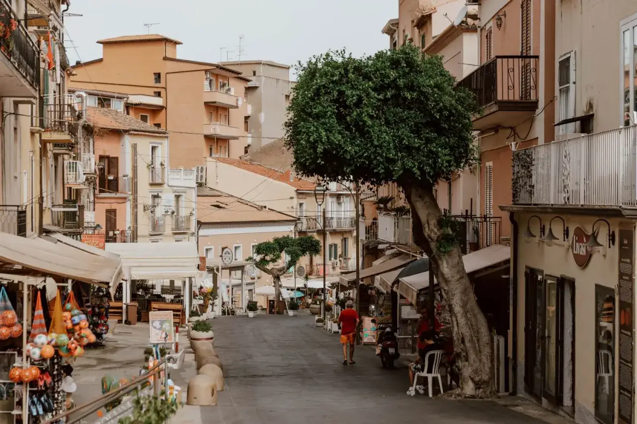 A man walks down a charming street in Tropea, lined with shops and colorful buildings. Discovering these things to do in Tropea is a delight.