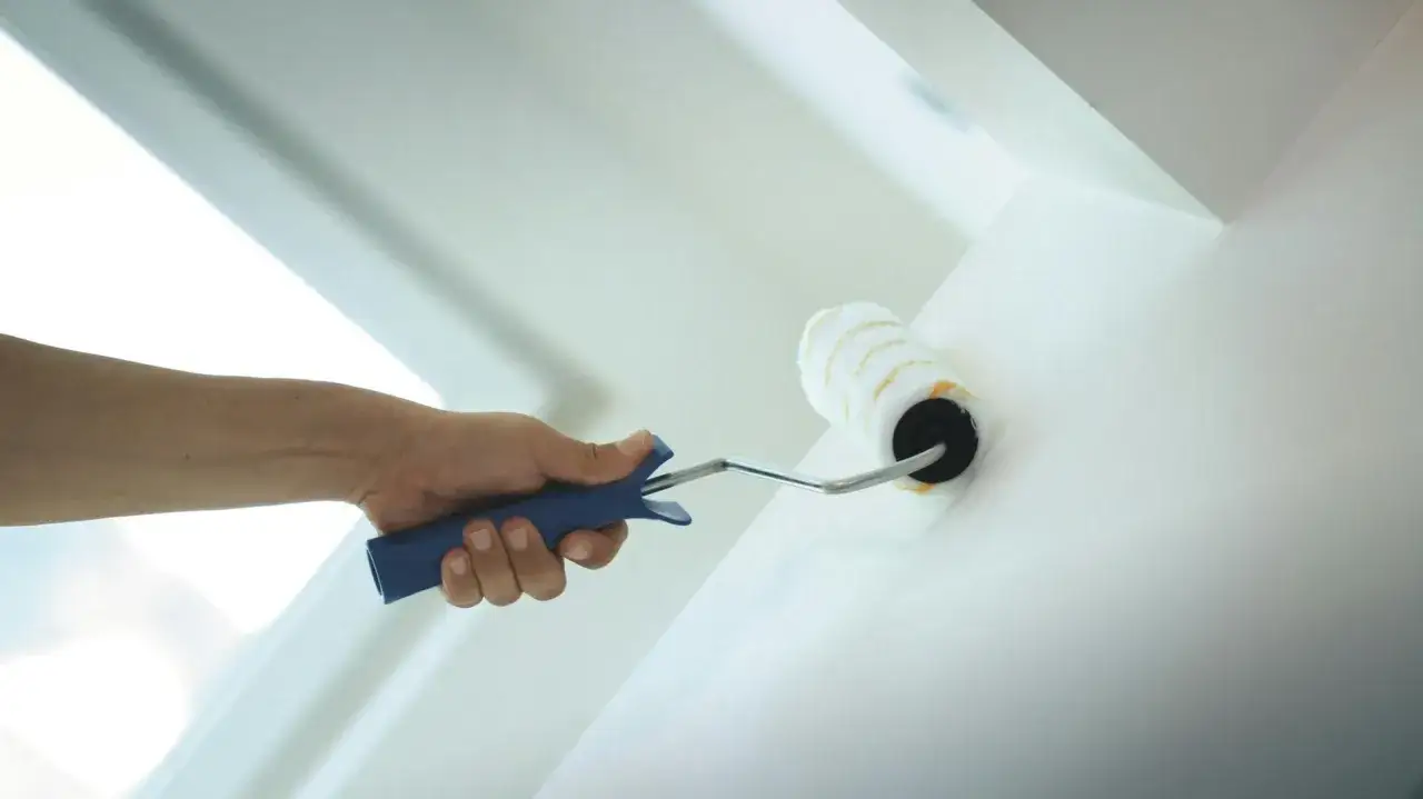 Hand streicht mit einer Farbrolle die Wand weiß. Der Putz wird frisch gestrichen, um dem Raum ein neues Aussehen zu verleihen.