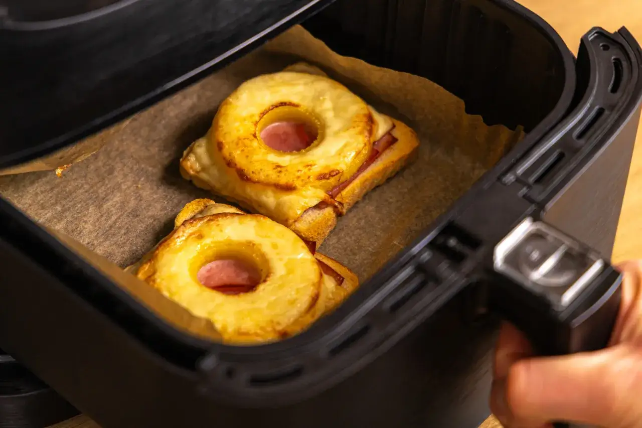 Zwei goldbraune Toast Hawaii mit Ananasringen und Schinken in der Airfryer-Schublade, bereit zum Genießen.