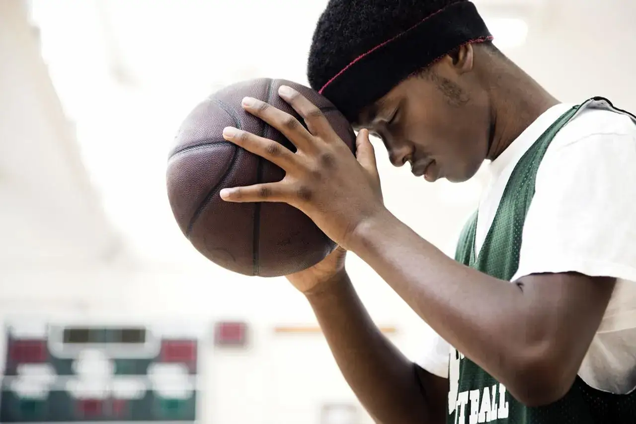 Giovane giocatore di basket con la fronte appoggiata sulla palla, concentrato. Un vero mental coach sportivo lo aiuta a trovare la forza interiore.