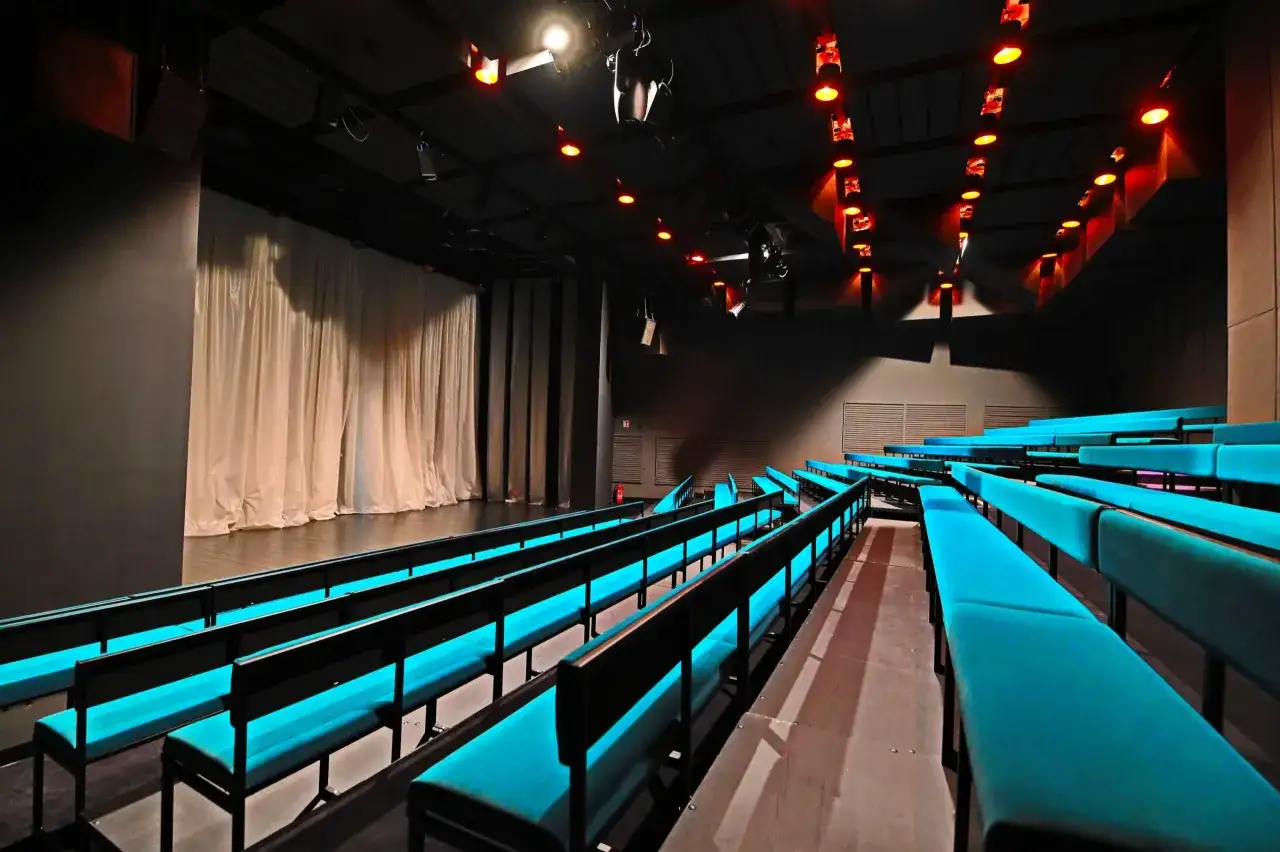Widownia Teatru Capitol z turkusowymi siedzeniami i sceną z białymi zasłonami. Ciemne wnętrze rozświetlają czerwone reflektory.