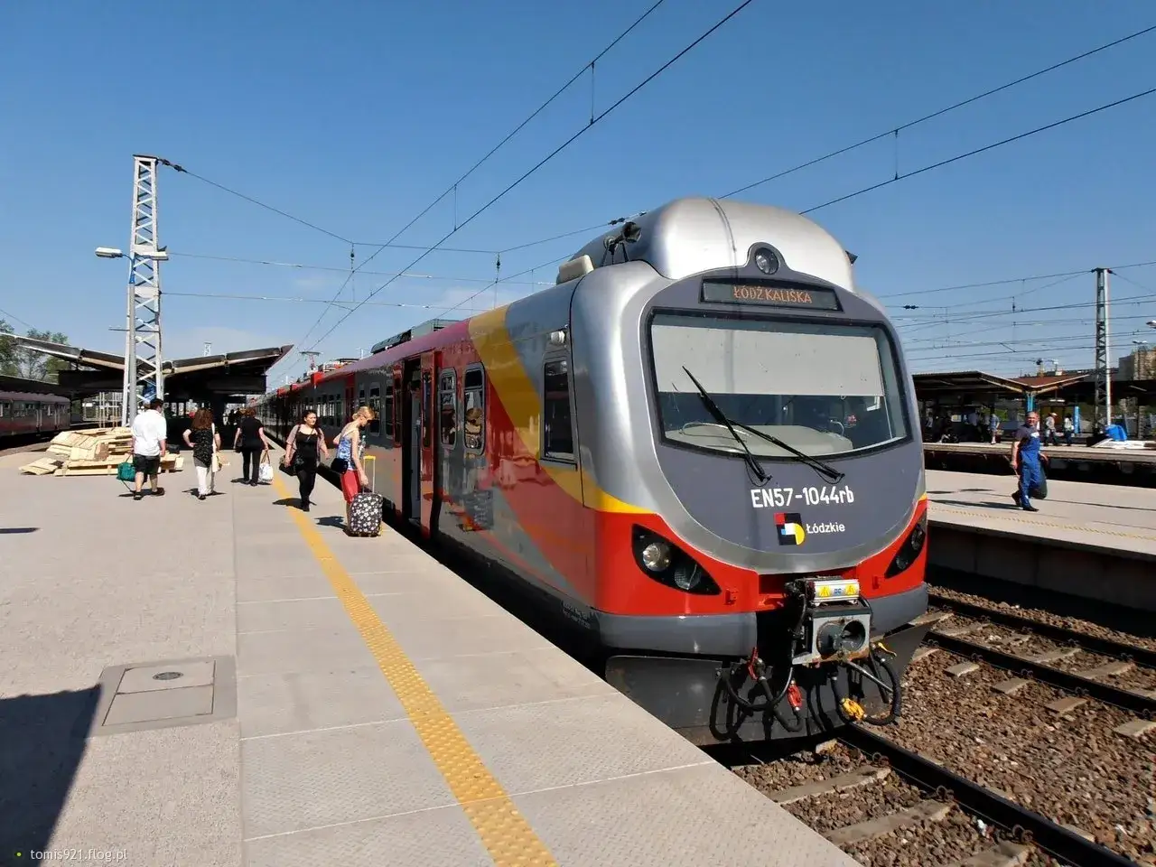 Nowoczesny pociąg EN57-1044rb Ł&oacute;dź Kaliska stoi na peronie. Pasażerowie z bagażami czekają na podr&oacute;ż.