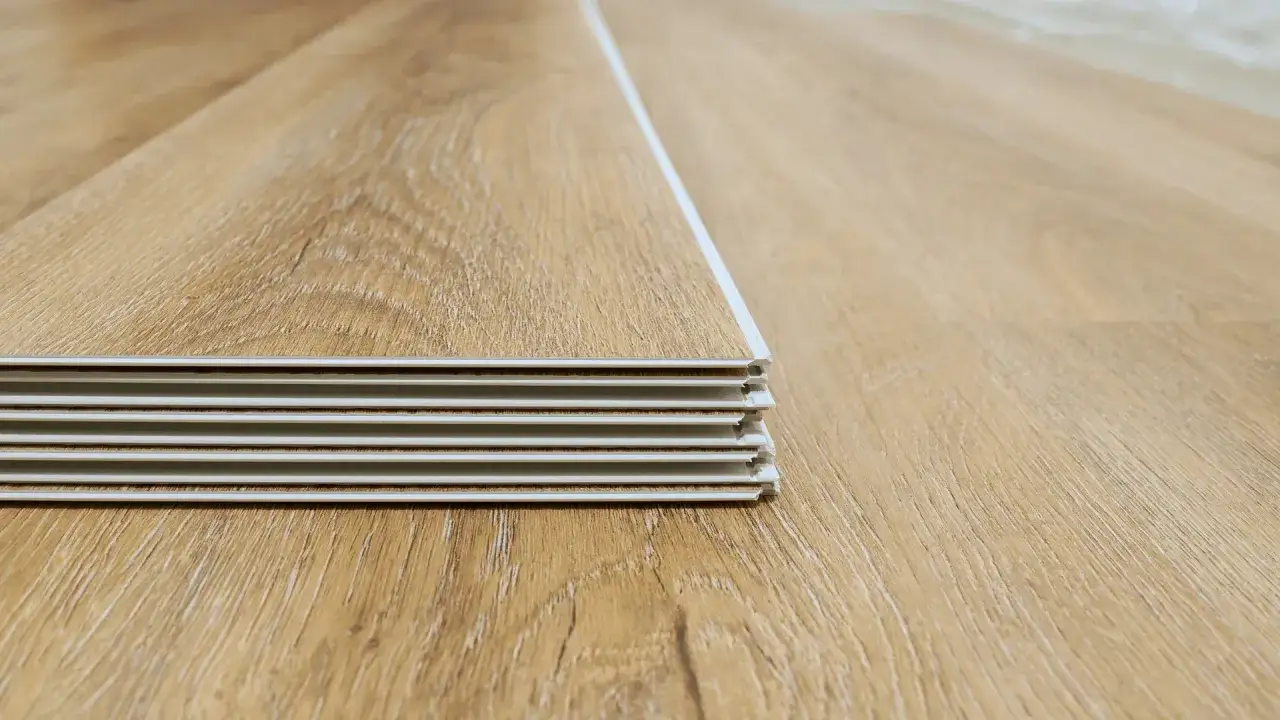 Stack of light brown wood-look planks with a visible interlocking edge, ready for drop and lock flooring installation.