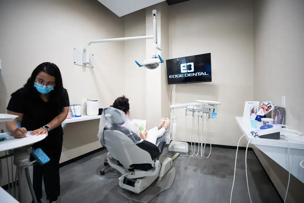 Dentystka notuje, pacjentka w fotelu przegląda materiały o tym, jak wybielić zęby. Na ekranie logo Edge Dental.