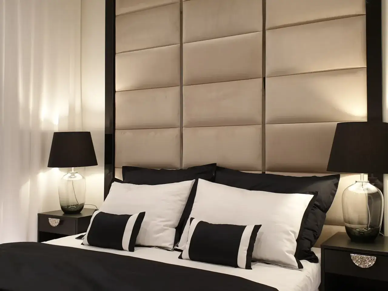 Elegancka sypialnia w stylu hotelowym z pikowanym zagłówkiem, czarnymi lampkami nocnymi i pościelą w kontrastowych barwach.
