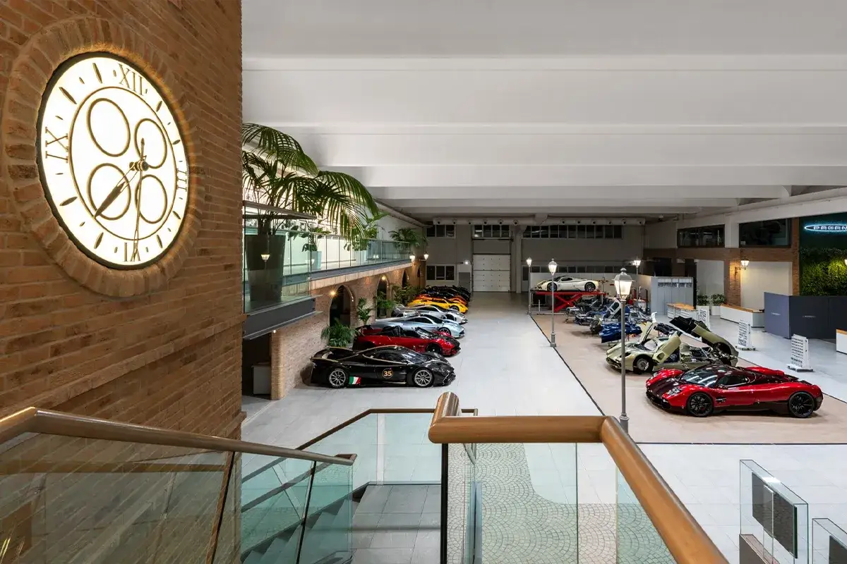 Eine beeindruckende Sammlung von Pagani-Supersportwagen in einer modernen Halle. Ein großes Wanduhr mit römischen Ziffern zeigt die Zeit an.