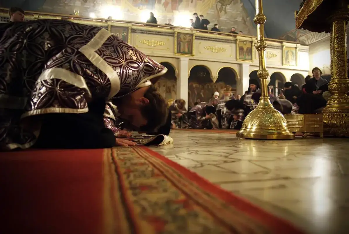 A man in ornate robes performs christian prostration in a church, bowing low to the floor.