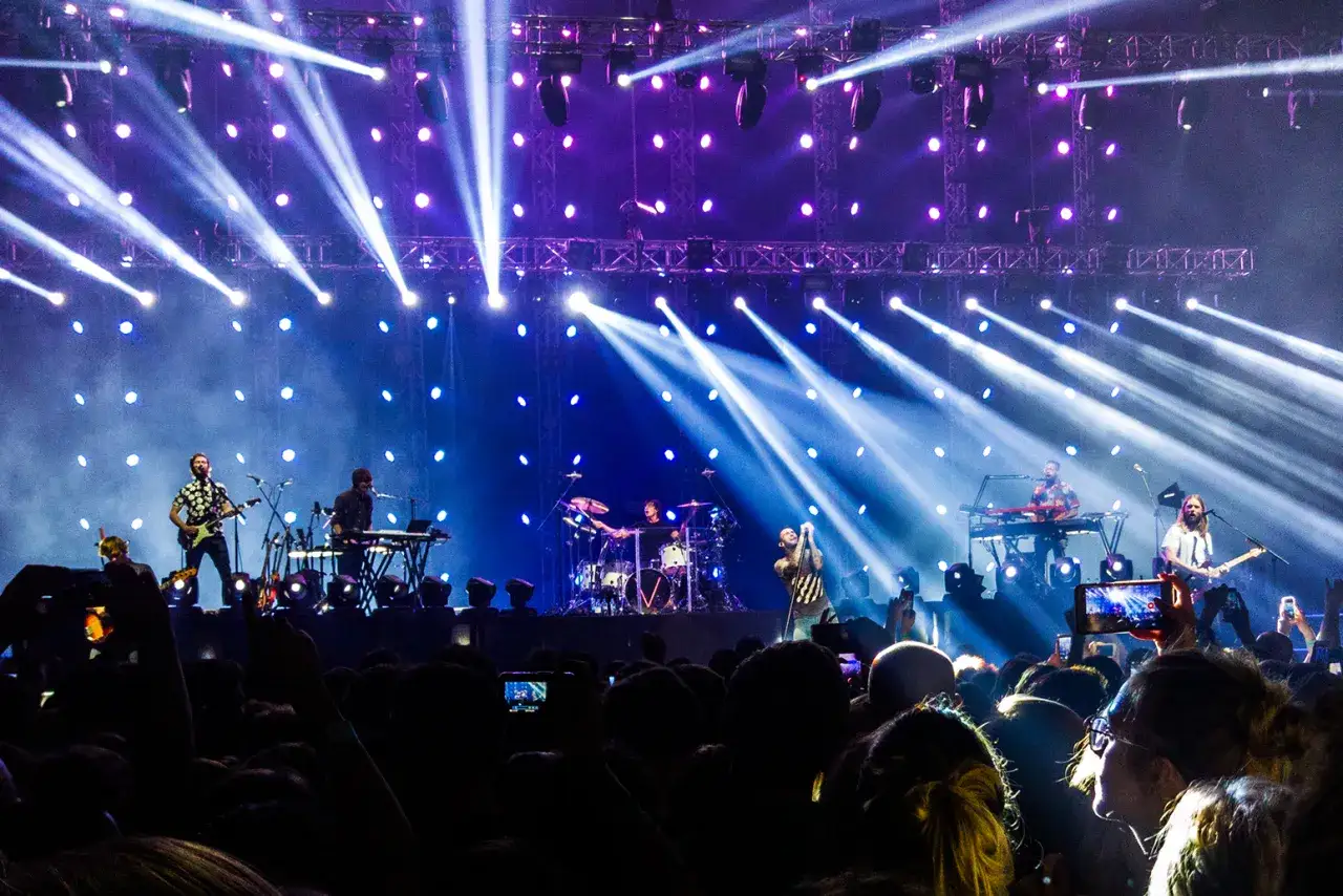 Koncert Maroon 5 w pełnym blasku świateł. Zespół gra na scenie, a tłum bawi się w rytm muzyki.