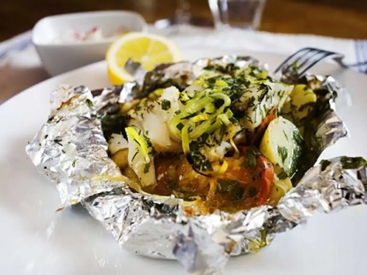 En h&auml;rlig fisk i folie med potatis, tomat och &ouml;rter, serverad med en citronklyfta.
