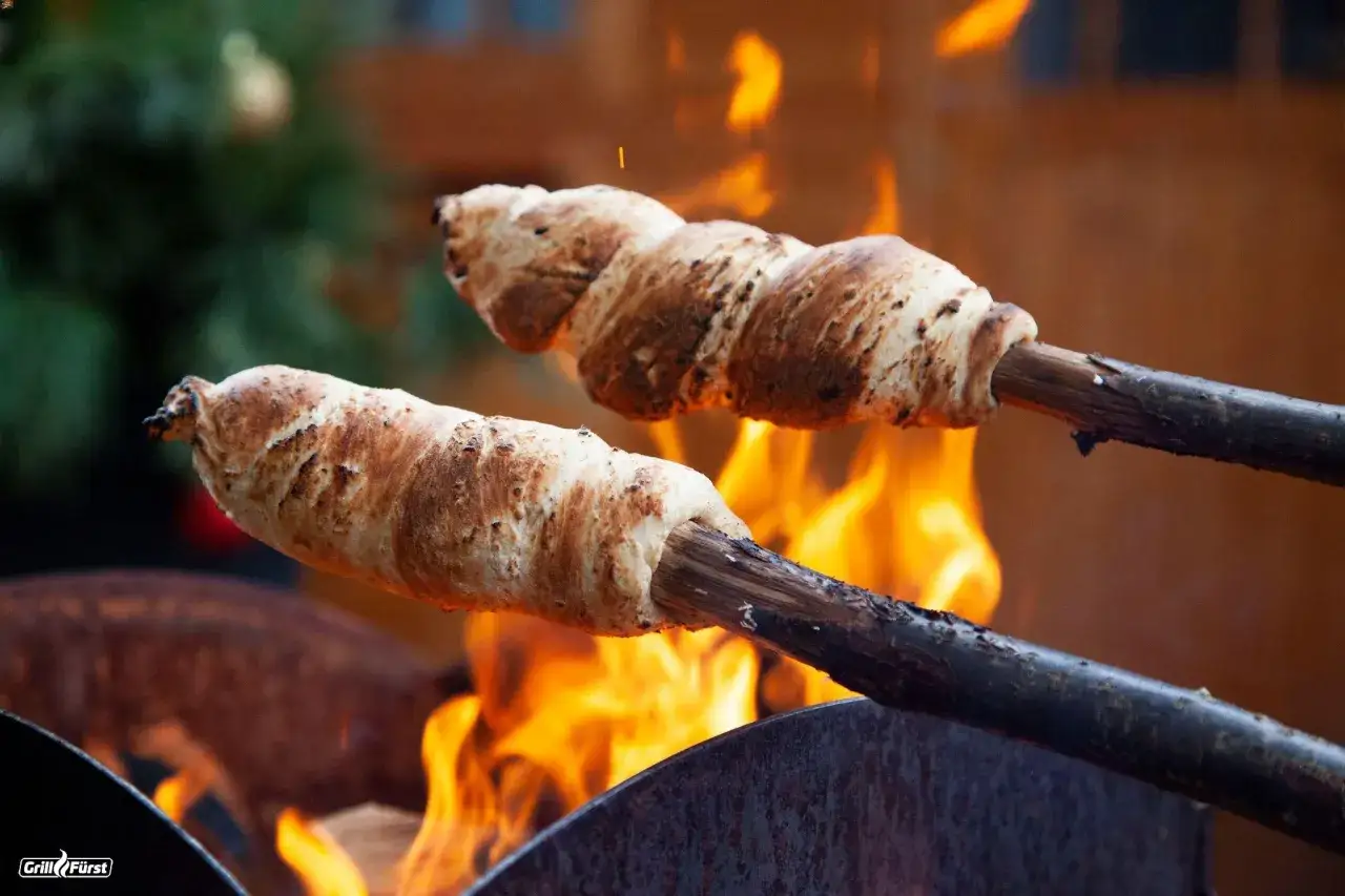 Zwei Stockbrote mit frischer Hefe werden über offenem Feuer gebacken. Sie sind goldbraun und knusprig.