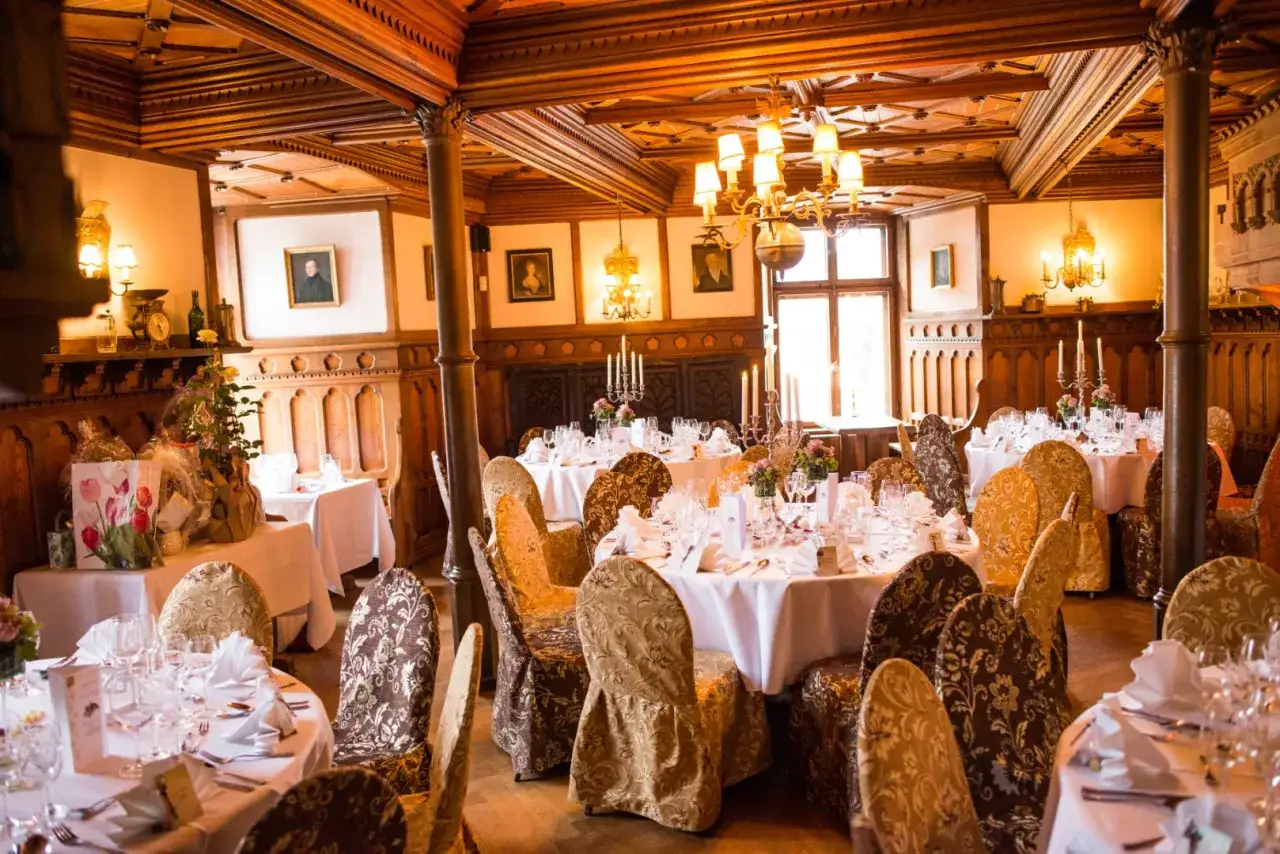 Festlich gedeckte Tische in einem holzgetäfelten Raum, bereit für eine mittelalterliche Hochzeit.
