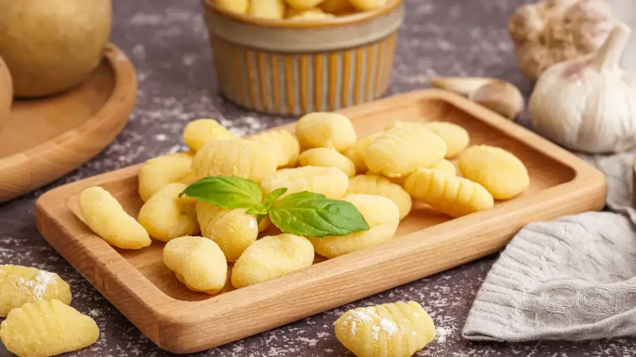 Świeże, domowe gnocchi na drewnianej desce, gotowe do przygotowania według ulubionego gnocchi przepis. Obok czosnek i bazylia.