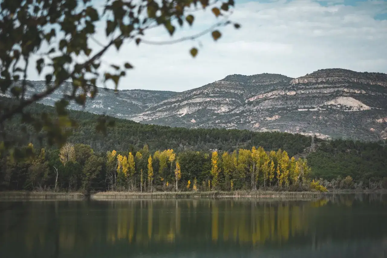 Reflejos otoñales en el lago, un preludio al montsec bikepacking loop. Montañas y bosques cubren la orilla.