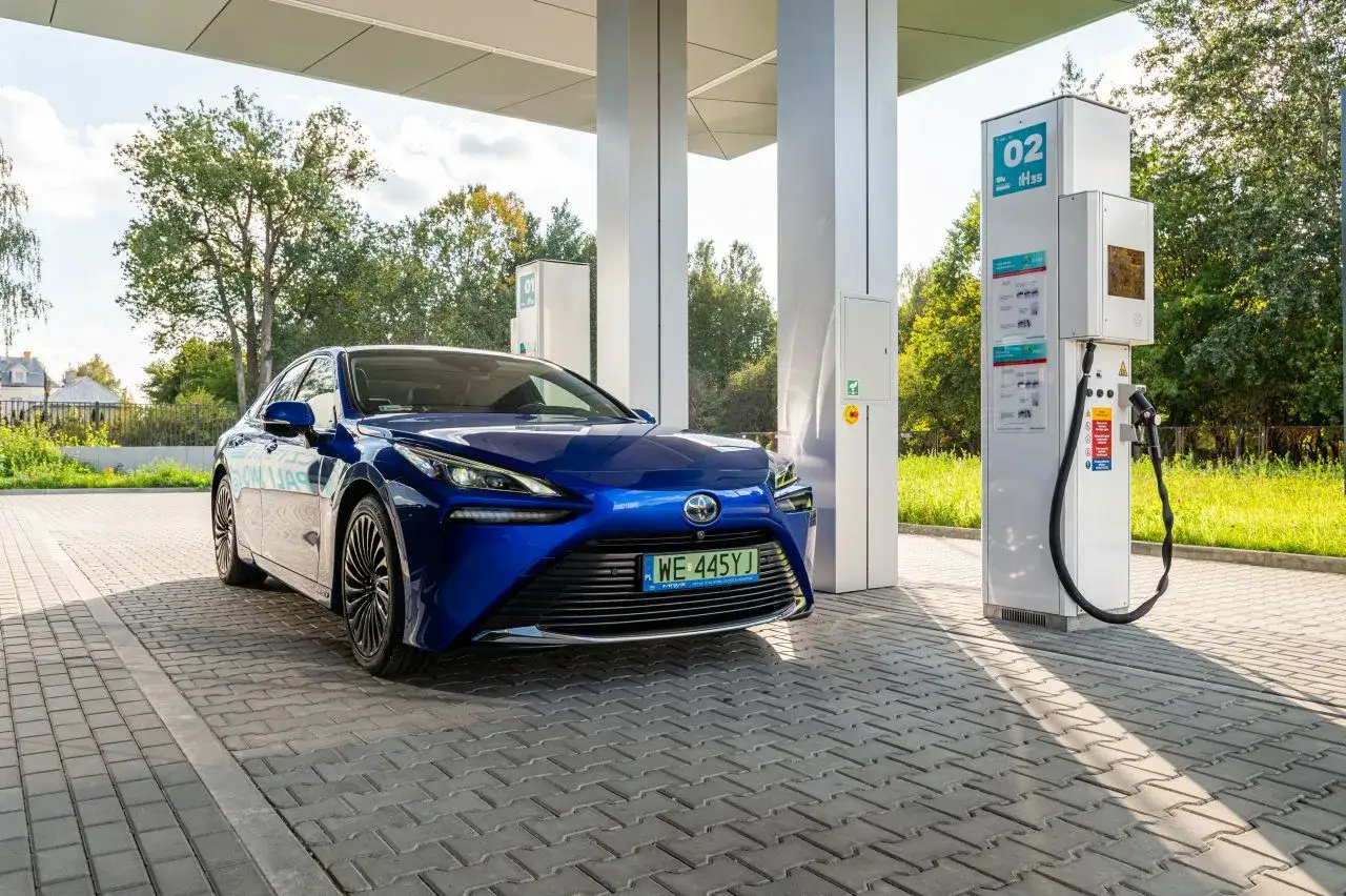 Niebieska Toyota Mirai na stacji tankowania wodoru. Długi zasięg tego auta pozwala na swobodne podróżowanie.