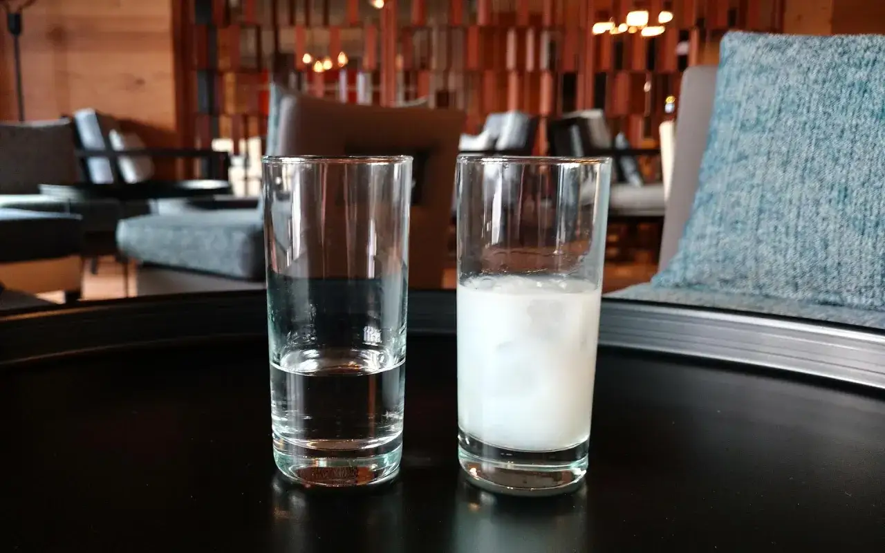 Zwei Gl&auml;ser auf einem Tisch. Eines mit Wasser, das andere mit Ouzo, der milchig tr&uuml;b wird. Typischerweise hat Ouzo 37,5% bis 50% Alkohol.