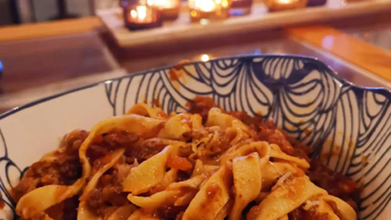 Herzhaftes Pasta Ragu in einer dekorativen Schüssel, im Hintergrund Kerzenlicht.