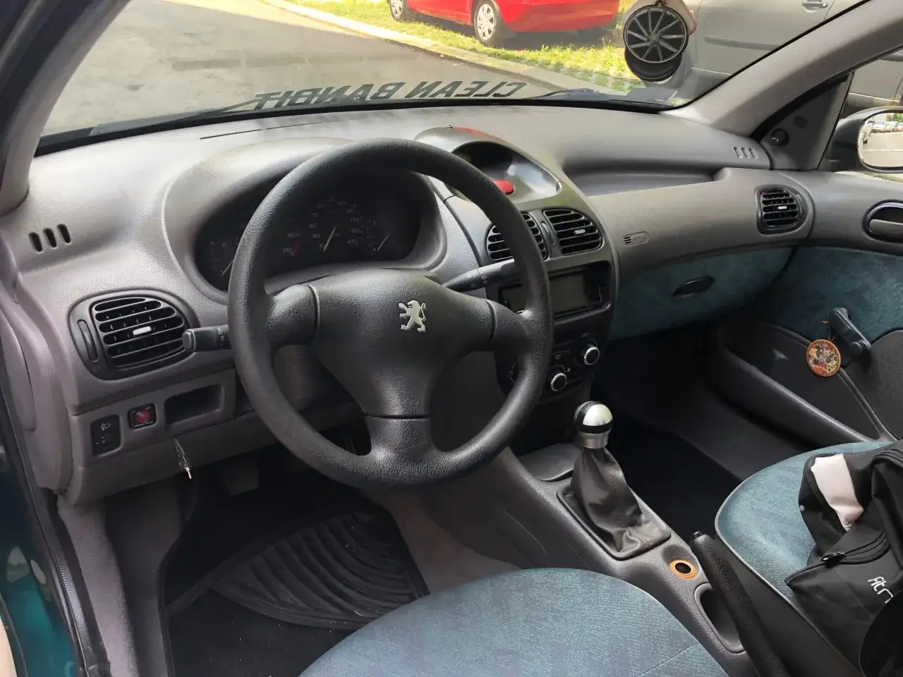 Wnętrze Peugeot 206 Plus z czarną kierownicą, deską rozdzielczą i siedzeniami. Widoczny lewarek zmiany biegów i radio.