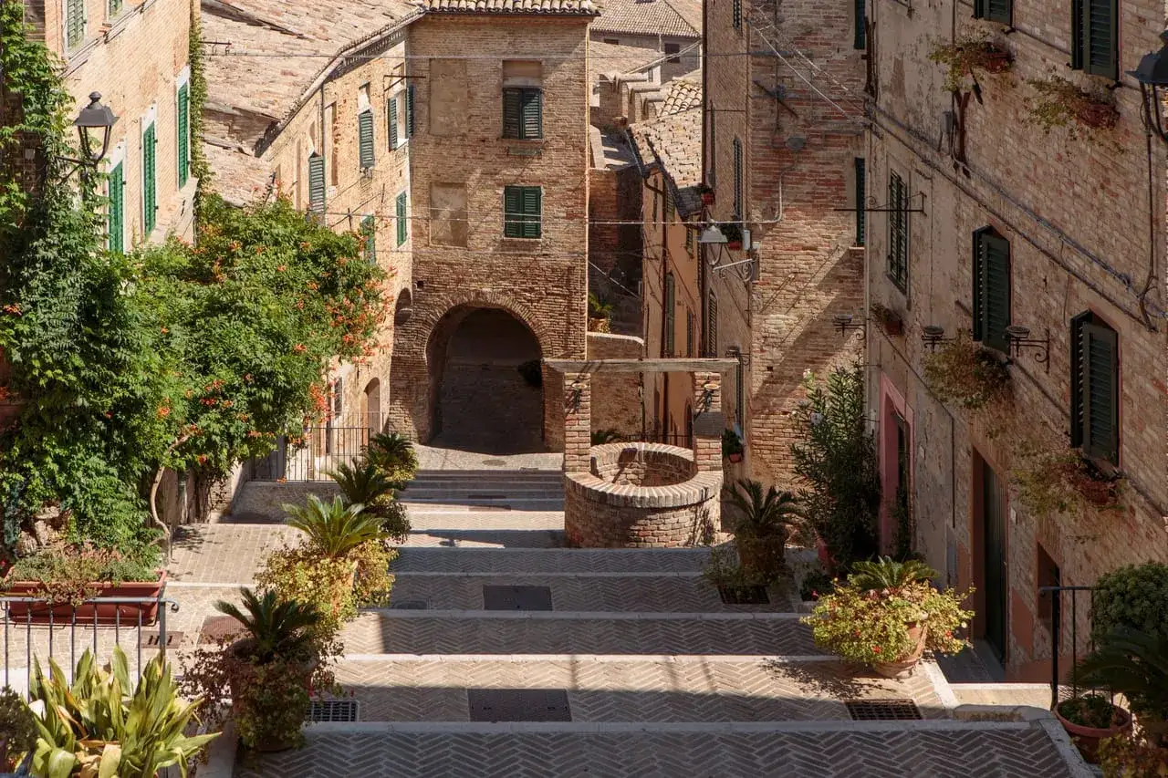 Scalinata in pietra a Corinaldo, dove si trova questo borgo medievale con case in mattoni e vegetazione rigogliosa.