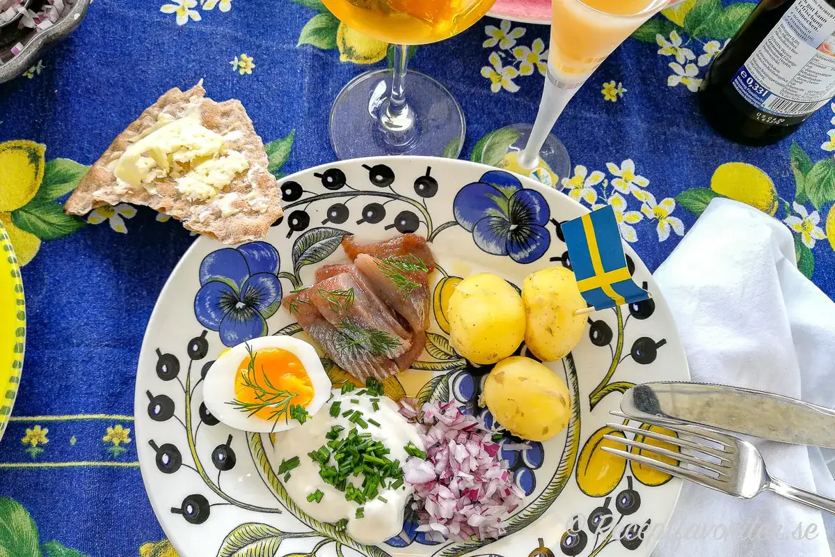 En tallrik med sill, potatis, &auml;gg och gr&auml;ddfil. En svensk flagga vajar stolt. Perfekt mat midsommar!