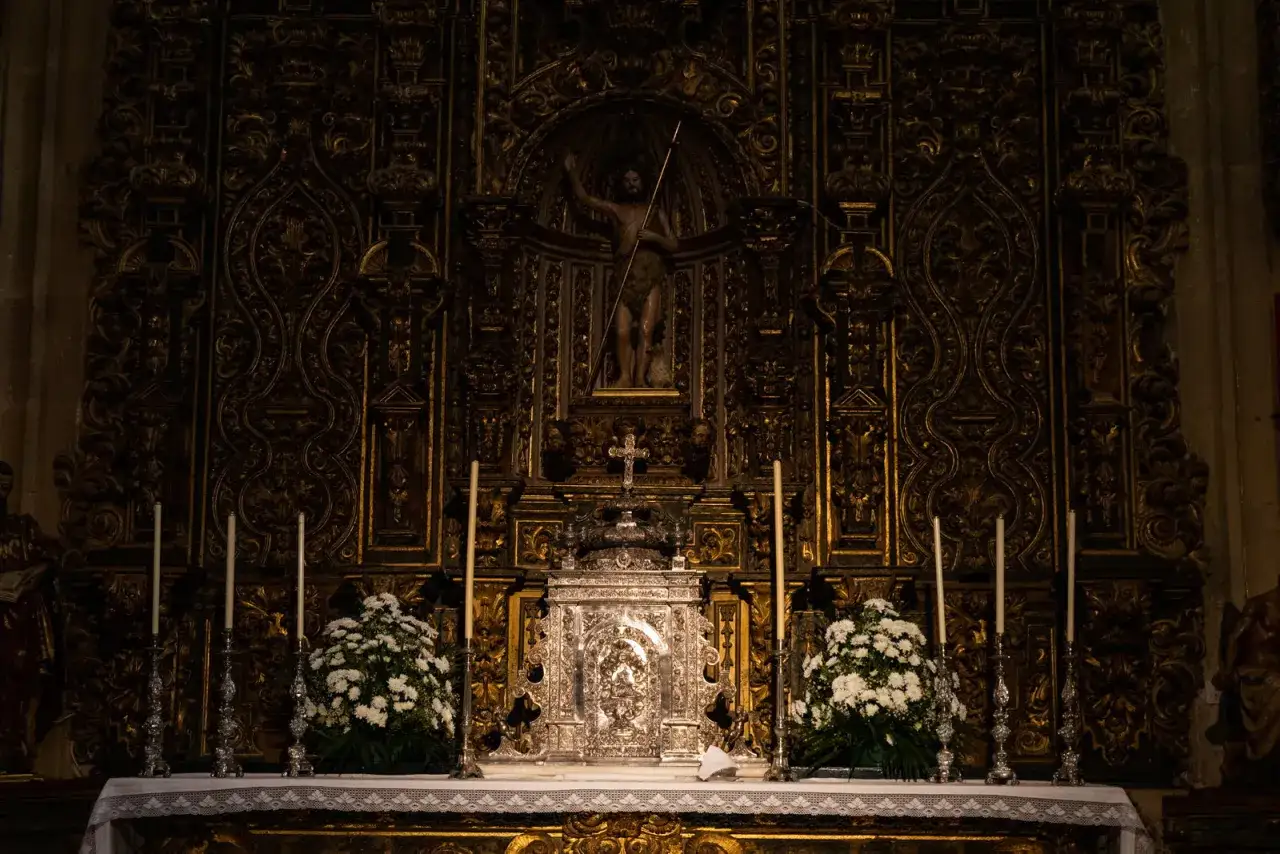 Retablo dorado con figura central de San Juan Bautista, un ostensorio plateado y flores blancas. Una joya barroca, la capilla Sixtina extremeña.
