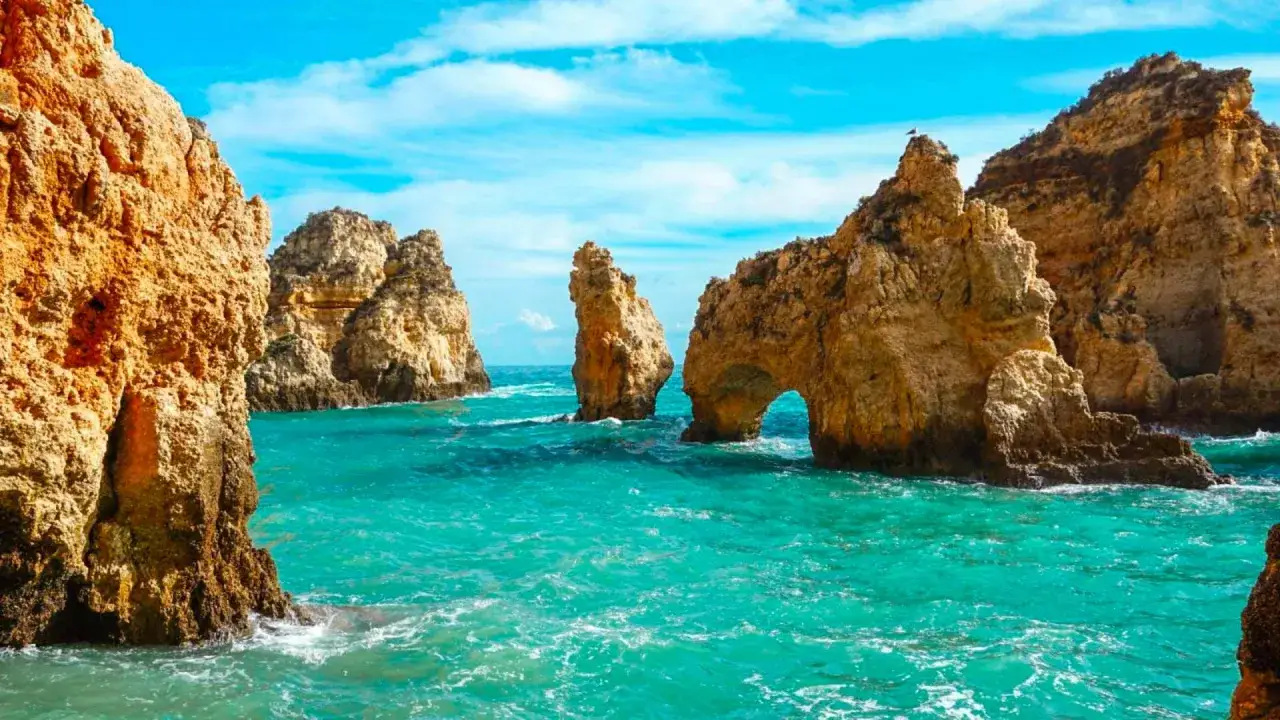 Felsformationen ragen aus dem t&uuml;rkisfarbenen Meer bei Lagos, Portugal, empor. Ein nat&uuml;rlicher Felsbogen ist sichtbar.