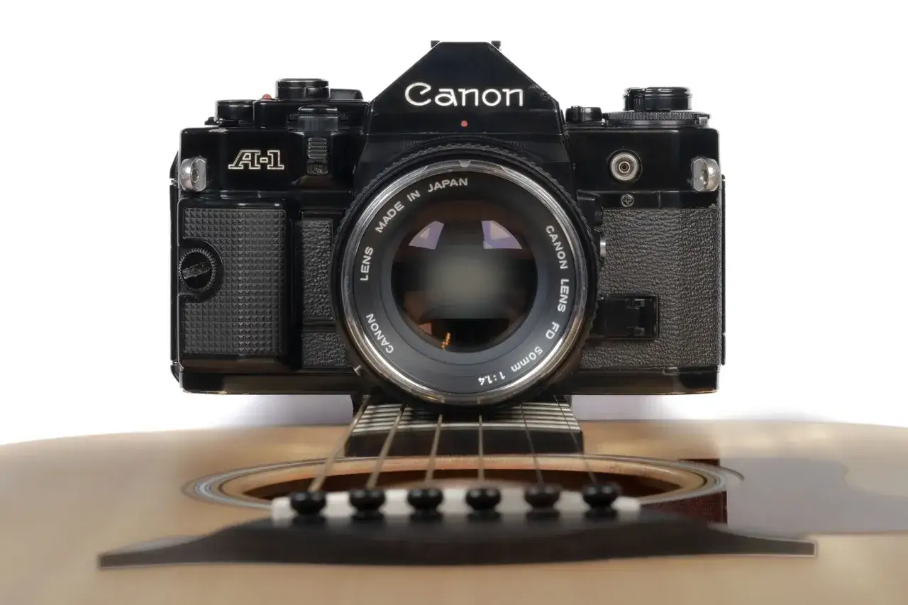 En svart Canon A-1 kamera vilar p&aring; en akustisk gitarr.