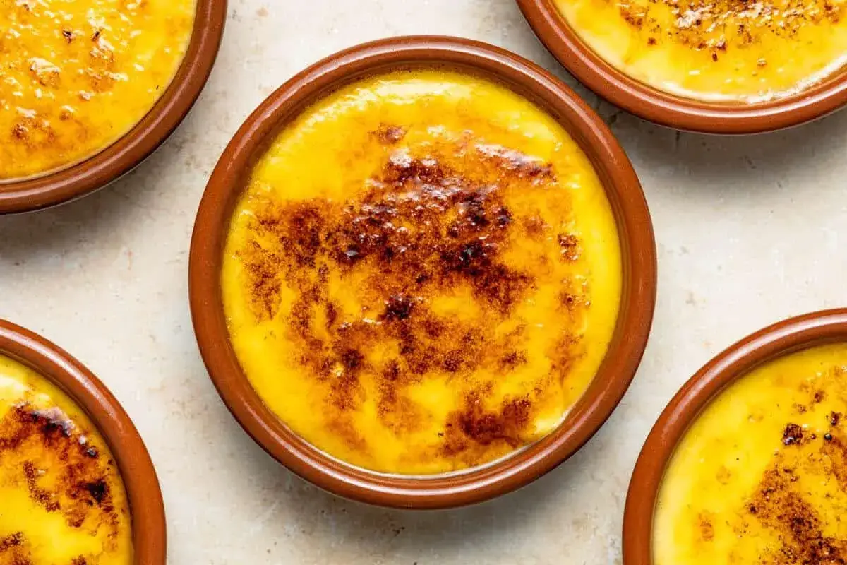 Flera krämiga crema catalana i bruna skålar, med karamelliserat socker på toppen.