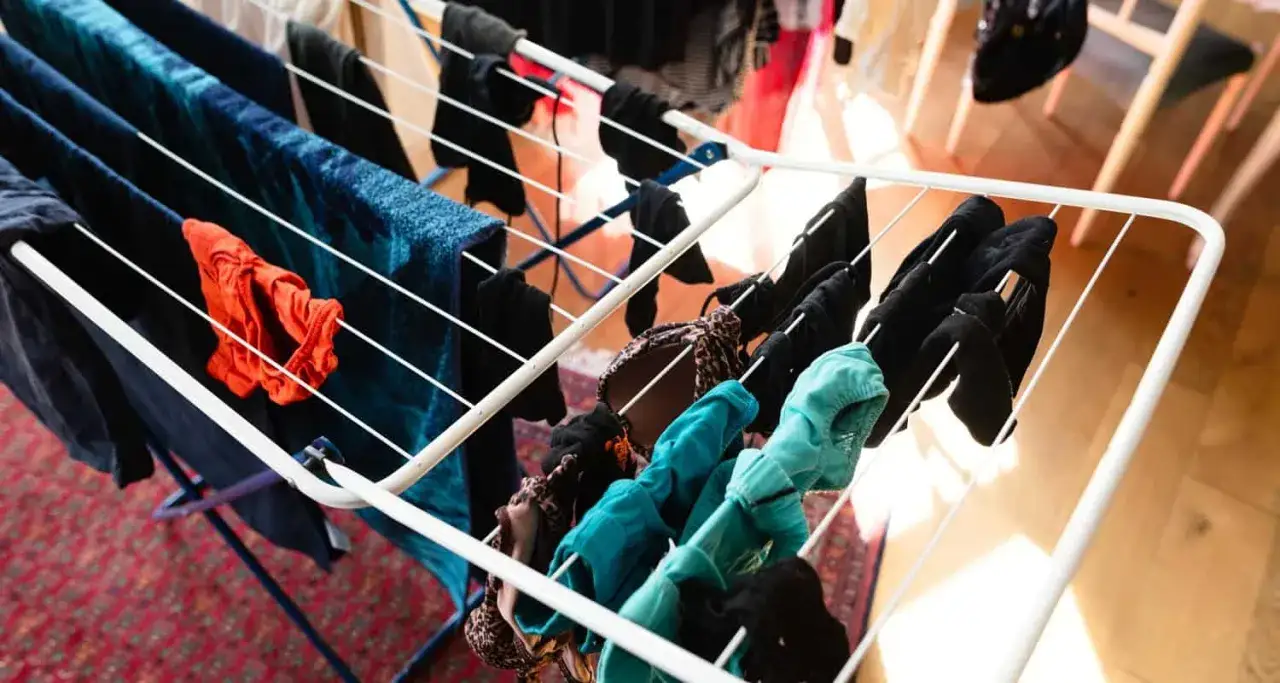 Wäscheständer mit bunter Kleidung, darunter ein rotes Oberteil und blaue Handtücher. So können die **Hose schnell trocknen**.