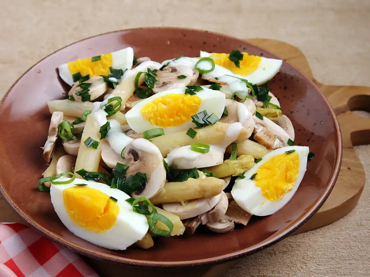 Ein köstlicher Spargelsalat mit Ei, Pilzen und Frühlingszwiebeln auf einem braunen Teller.