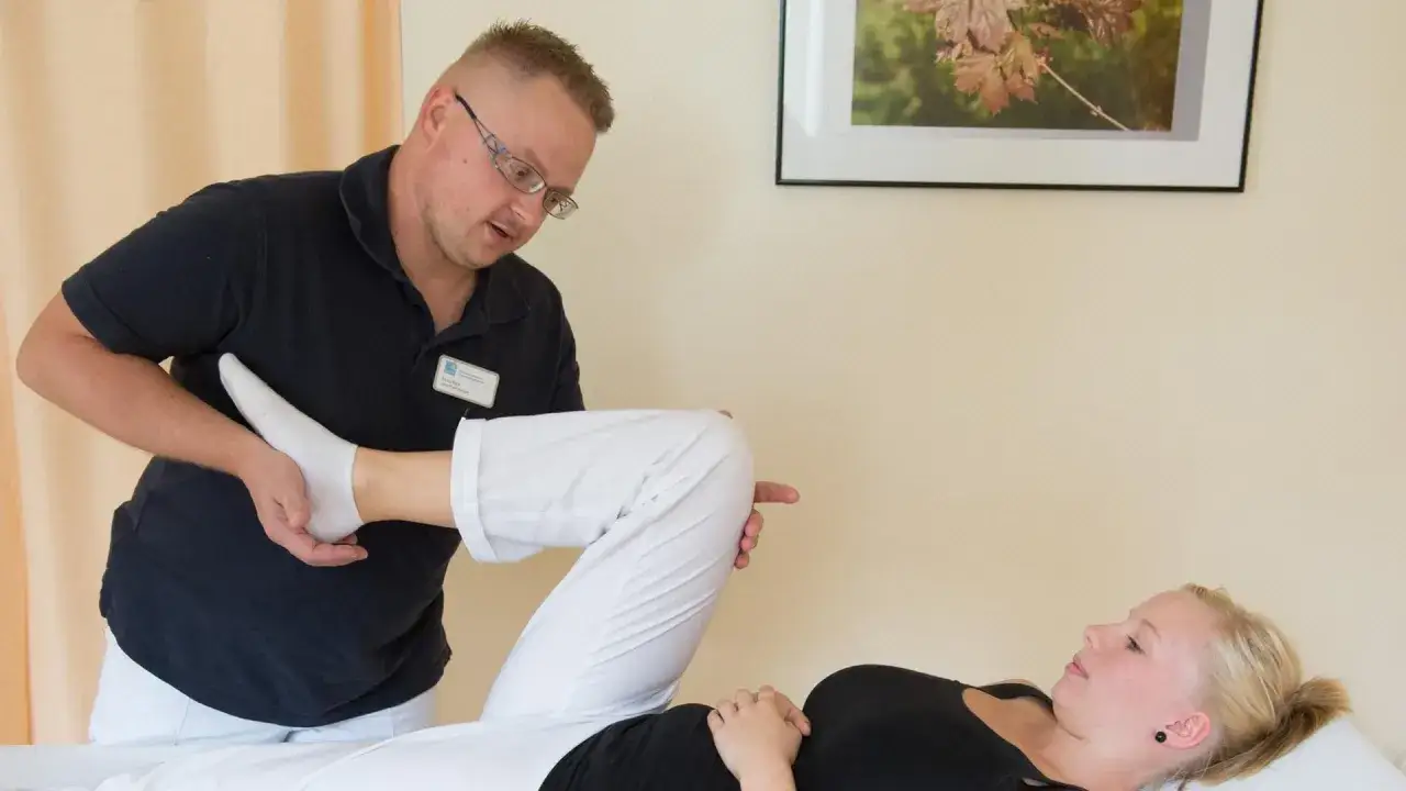 Physiotherapeut unterstützt Patientin bei der Bewegung des Beins zur Schmerzbewältigung.