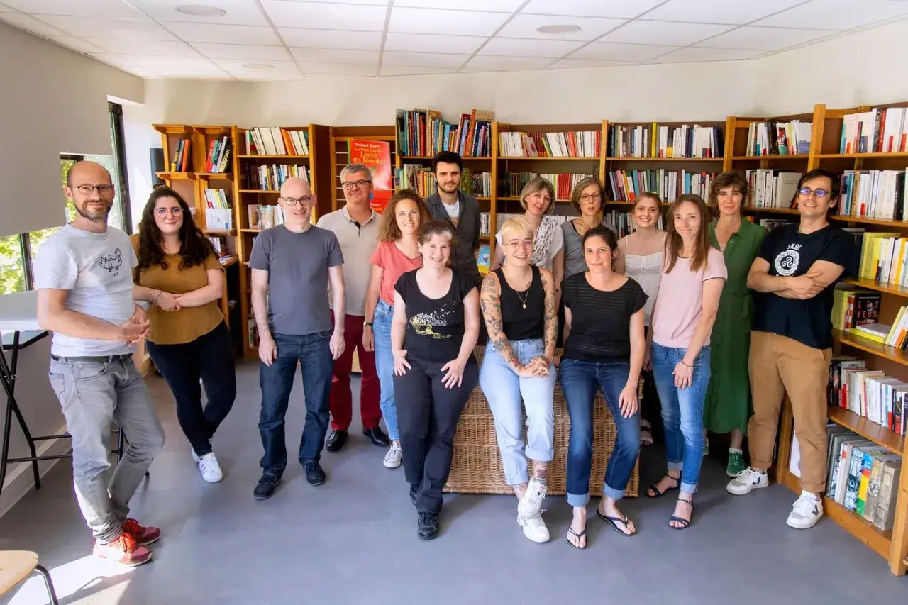 Une équipe souriante pose devant des étagères remplies de livres pour adolescents.