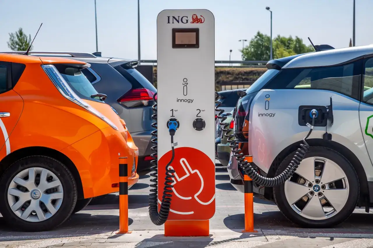 Pomarańczowy i srebrny samochód elektryczny ładuje się przy stacji. Dofinansowanie 