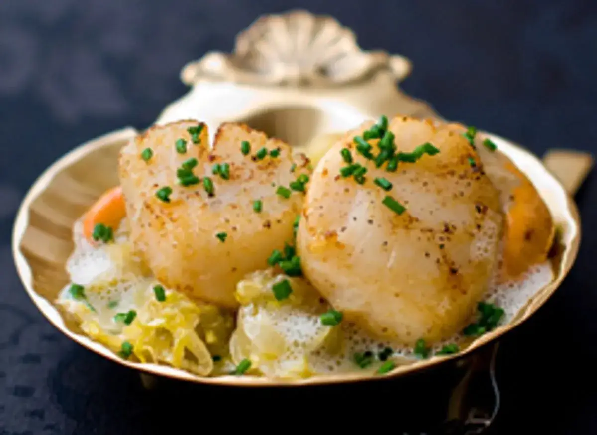 Saint-Jacques poêlées sur lit de poireaux fondants, une recette entrée originale et raffinée, garnie de ciboulette fraîche.