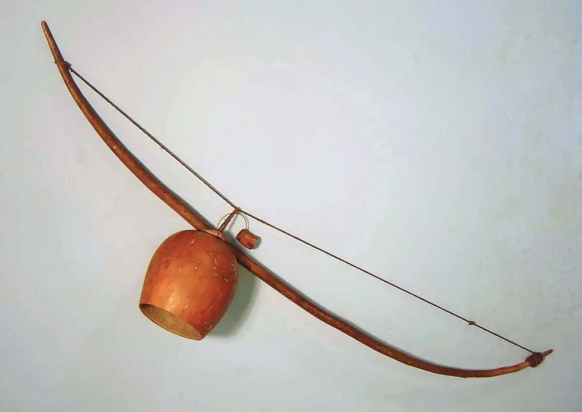 Drewniany łuk muzyczny instrument z tykwą jako pudłem rezonansowym, gotowy do wydobycia rytmicznych dźwięków.