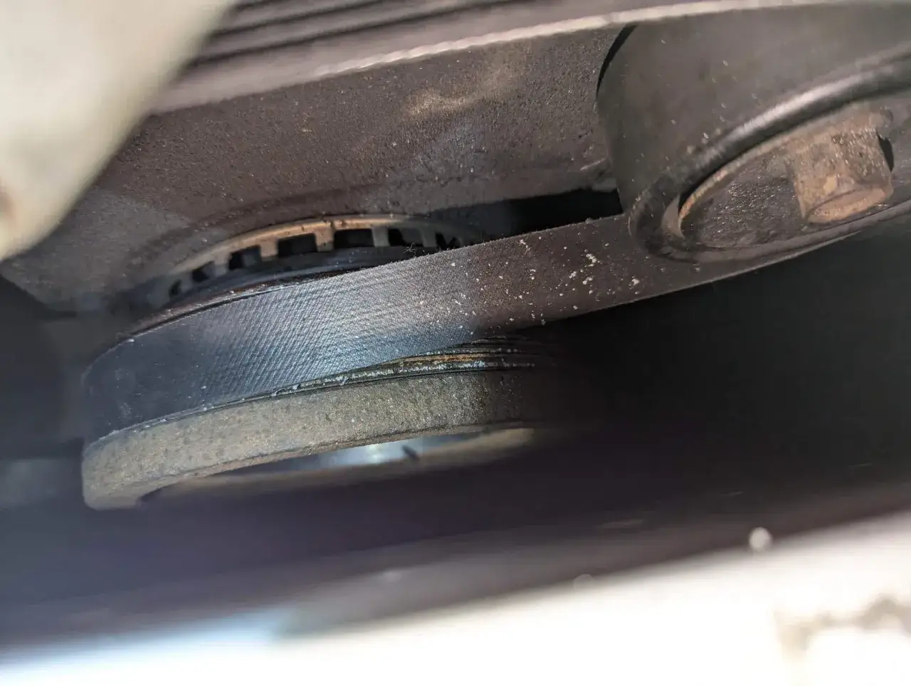 Close-up of a car's serpentine belt wrapped around a pulley, likely part of the harmonic balancer, which helps absorb engine vibrations.