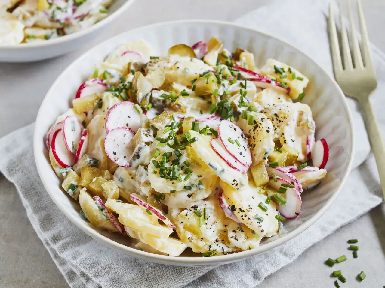 Kartoffelsalat mit Joghurt, Radieschen und Schnittlauch, garniert mit Pfeffer. Ein leichter und frischer Genuss.