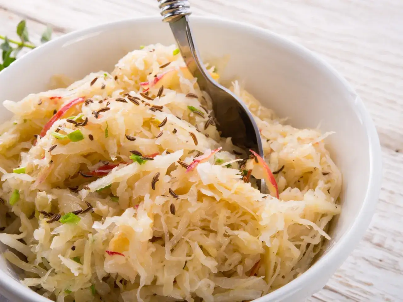 Schüssel mit Sauerkraut, Kümmel und Apfelstücken. Ein Löffel ragt hinein. Vielleicht ist das Sauerkraut zu sauer?
