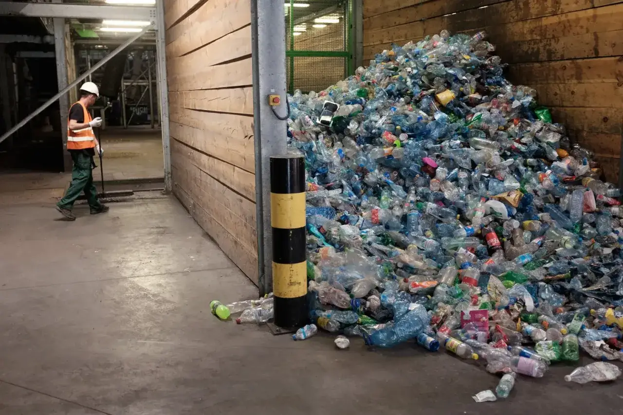 G&oacute;ra plastikowych butelek czeka na recykling w Polsce. Pracownik w kamizelce obserwuje proces.