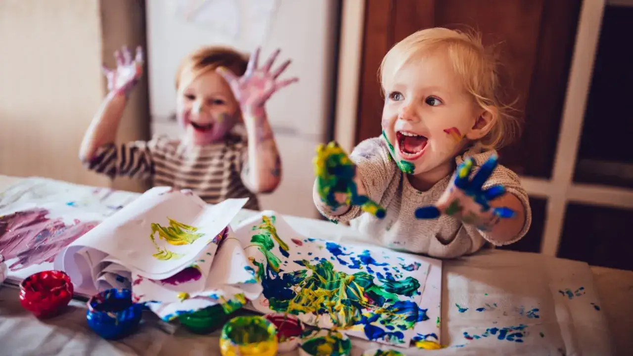 Niños felices disfrutando de manualidades con pintura de dedos, sus manos y caras llenas de color.