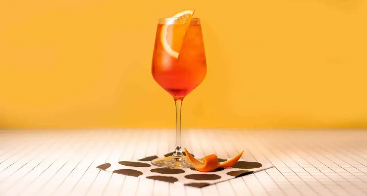 Ein Aperol Spritz mit Orangenscheibe und -spirale auf einem gepunkteten Tuch. Entdecke Aperol Spritz Varianten!