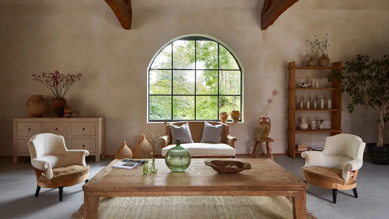 A cozy living room with rustic chic interior design, featuring a large arched window, wooden furniture, and earthy decor.