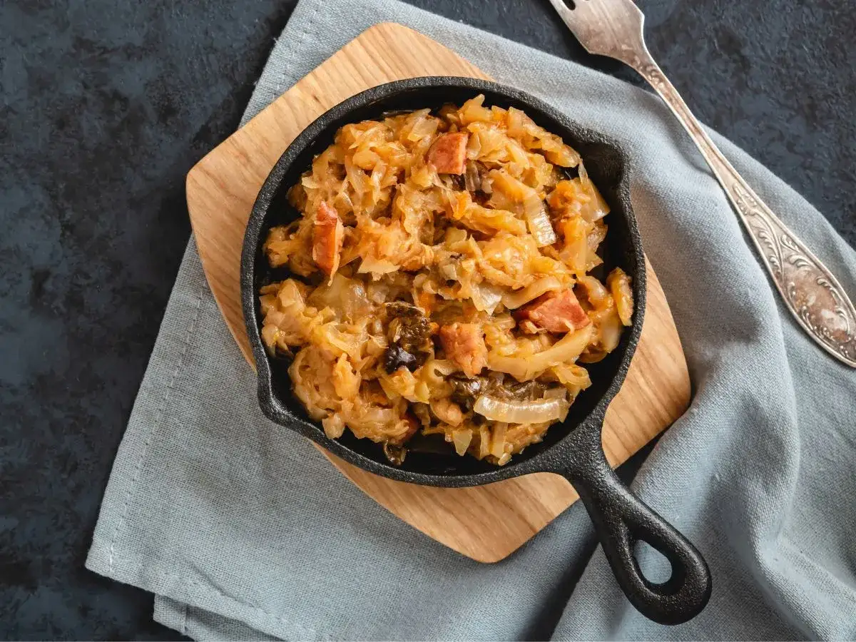 Pyszny bigos ze słodkiej kapusty z kawałkami kiełbasy i grzyb&oacute;w, podany w żeliwnej patelni.