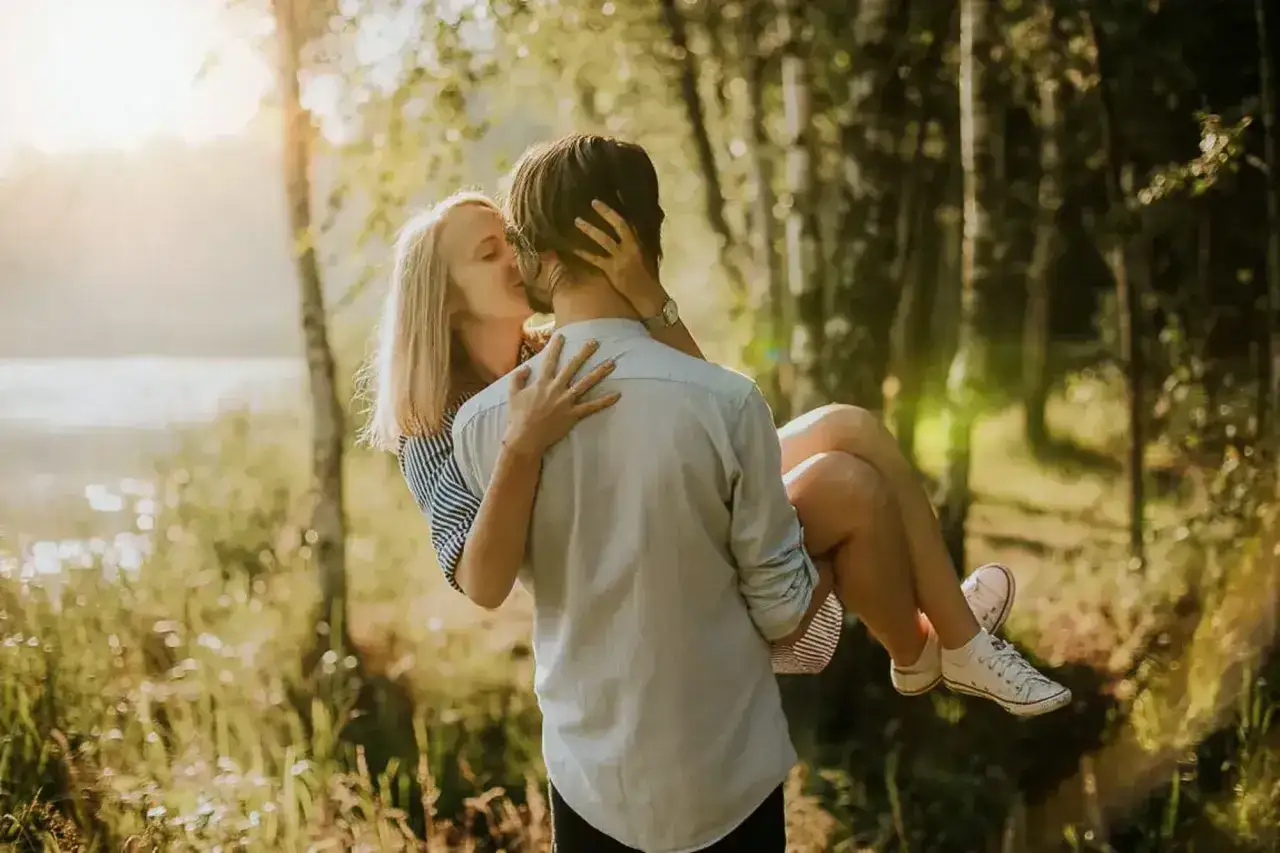 Para, który całuje się w lesie, to jak romantyczne sexting przykłady. Słońce przebija się przez drzewa, tworząc magiczną atmosferę.