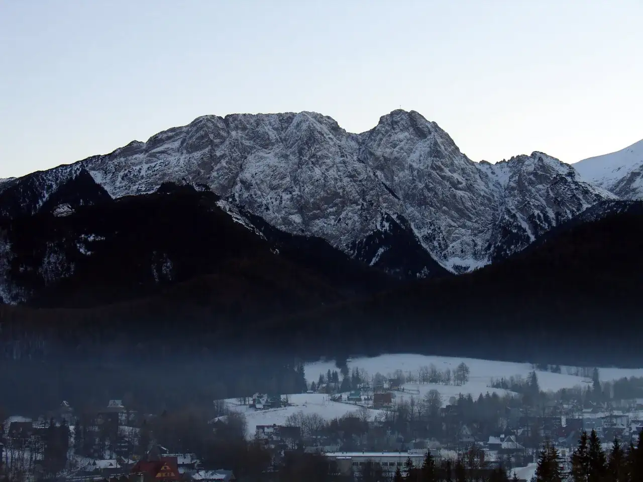Zimowy krajobraz z ośnieżonymi Tatrami w tle i zabudowaniami u podnóża. Widok na Tatry po angielsku, czyli po prostu