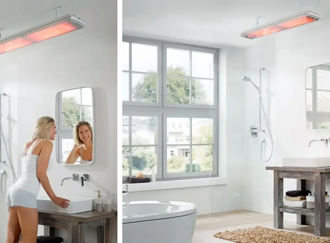 Une femme souriante se regarde dans le miroir d'une salle de bain moderne. Au-dessus, un appareil de chauffage infrarouge, une chaudi&egrave;re ou chauffe eau, diffuse une douce chaleur rouge.