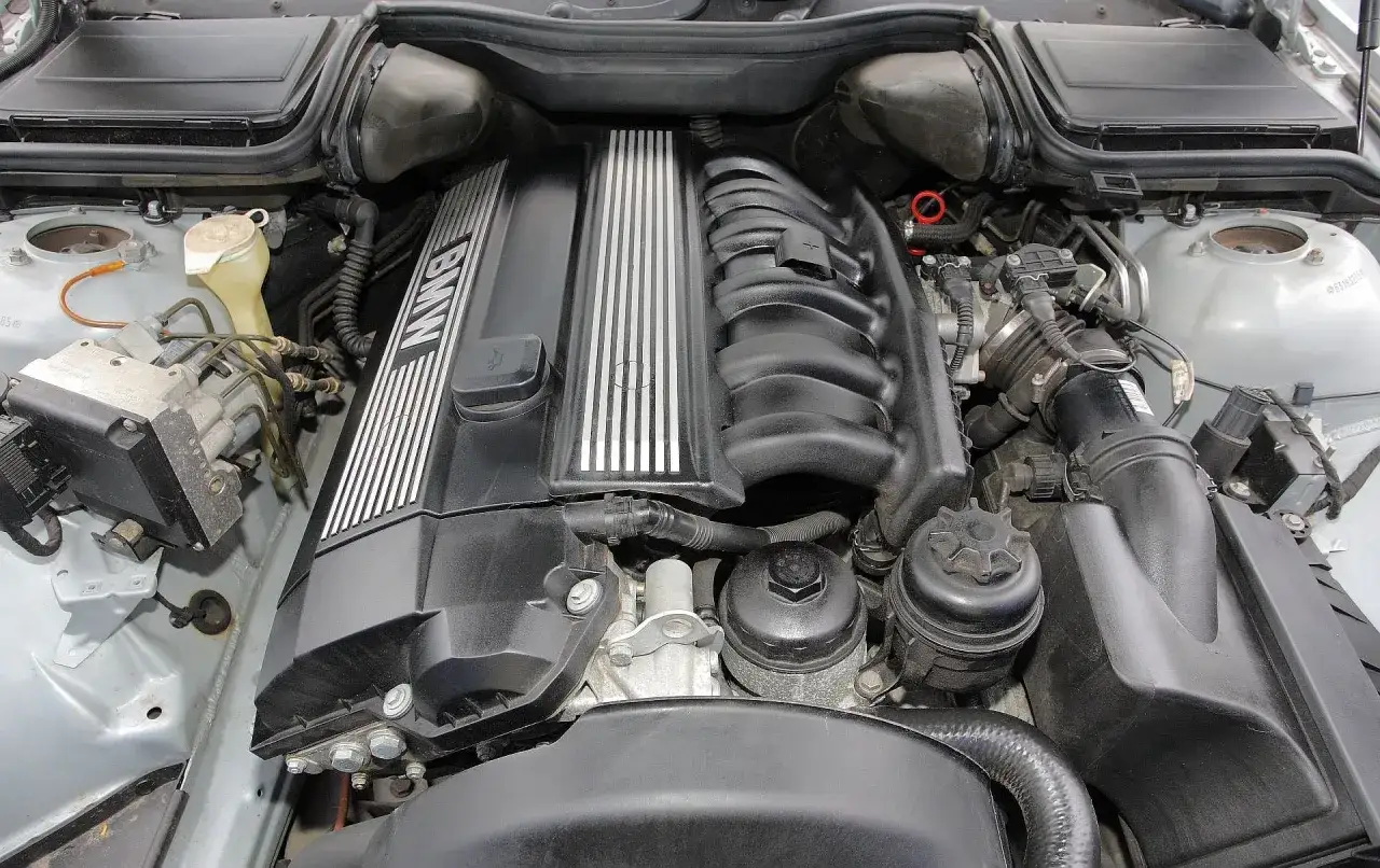 Silnik BMW E39, prawdopodobnie V8, z widocznym kolektorem dolotowym i pokrywą zaworów z napisem BMW.