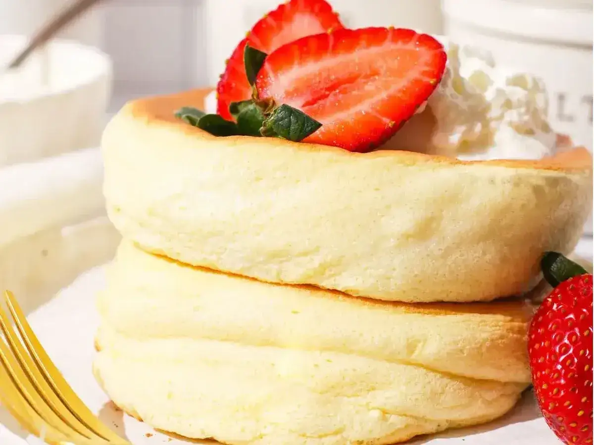 Une pile de crêpes japonaises moelleuses, garnies de fraises fraîches et de crème fouettée. Un délice léger et aérien.